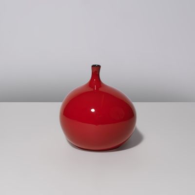 un vase rouge posé sur une table blanche