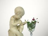 a statue of a boy sitting on a rock next to a vase of flowers