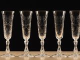 six empty champagne glasses lined up on a table against a black background