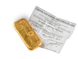 un gros plan d'un lingot d'or posé à côté d'un ticket de caisse sur une surface blanche