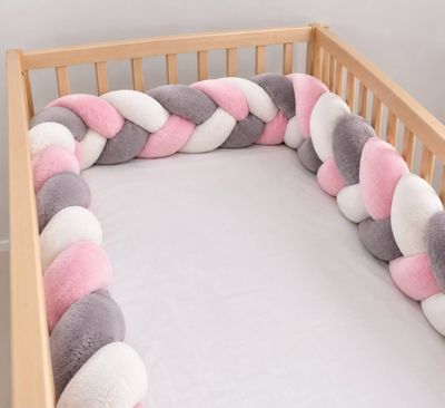 a crib with a pink, white and grey blanket on it