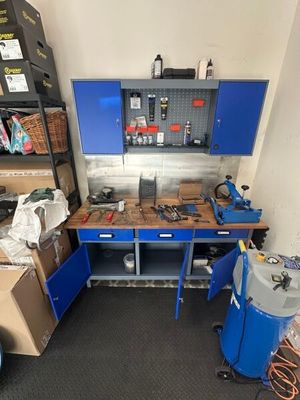 un établi bleu au milieu d'une pièce où s'entassent de nombreuses boîtes par terre