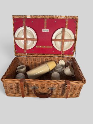 a wicker picnic basket with plates and cups in it