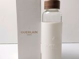 un flacon d'eau de Guerlain avec un bouchon en bois, posé devant une boîte blanche