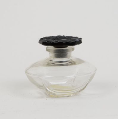 une petite bouteille en verre avec un bouchon noir posée sur une surface blanche