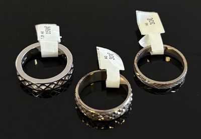 trois bagues en argent munies d'étiquettes, posées sur une surface noire