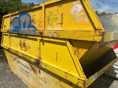une benne jaune recouverte de graffitis, dans un parking