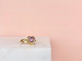 une bague en or ornée d'une pierre rose en forme de cœur posée sur un bloc de marbre