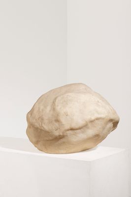 une sculpture représentant un rocher posé sur un socle dans une pièce blanche