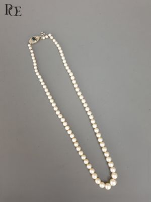 un collier de perles blanches muni d'un fermoir en argent, sur fond gris