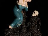 une figurine représentant une femme assise sur un rocher, tenant un crâne