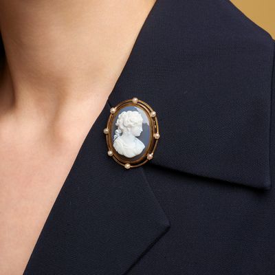 a close up of a woman wearing a black suit and a white cameo broocher