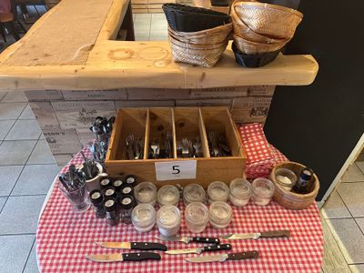 une table recouverte d'une nappe à carreaux rouges et blancs, sur laquelle se trouve une boîte en bois contenant des couverts