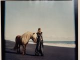 a woman standing next to a horse on the beach