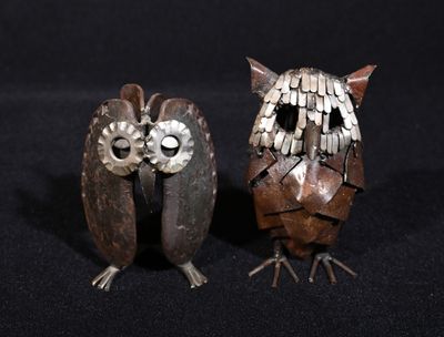 two metal owls sitting next to each other on a black surface