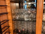 bottles and glasses are stacked on shelves in a wooden cabinet