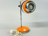 une lampe de table orange posée sur un pied en métal, avec un cordon blanc