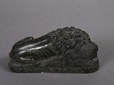 bronze statue of a lion resting on a rock on a gray surface