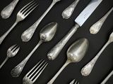 de nombreuses cuillères et fourchettes en argent posées sur une table noire