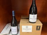deux bouteilles de vin posées sur des cartons, sur une étagère en bois