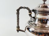 a silver tea pot with a handle on a table