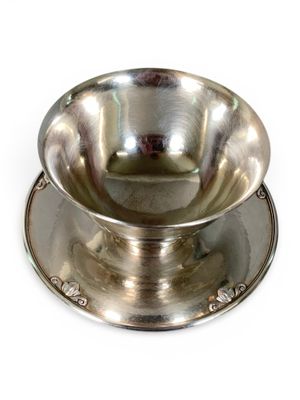 a silver bowl on a saucer on a white surface