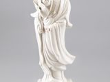 une statue blanche représentant une femme tenant une fleur, posée sur un socle doré
