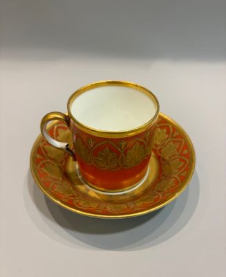 an orange and gold cup and saucer sitting on top of a white table