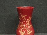 un vase rouge orné de motifs dorés, posé sur une surface noire