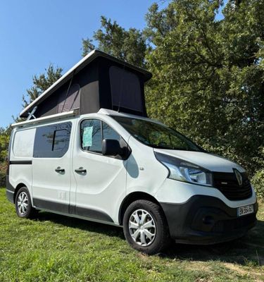 une camionnette blanche garée dans un champ, avec une tente posée dessus