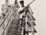 black and white photo of a man with a rifle standing on a set of stairs