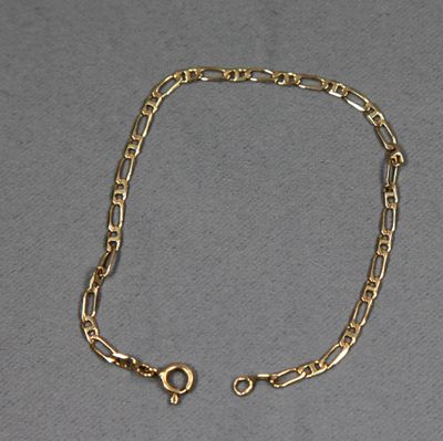 gros plan d'un bracelet en chaîne en or sur une surface grise