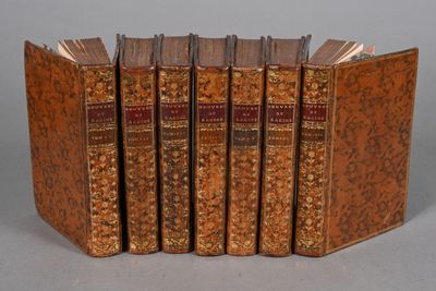 six antique books lined up in a row on a gray surface