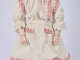 an antique doll with a white dress and bonnet is standing on a white surface