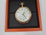 une montre de poche en or dans un écrin posé sur une surface blanche