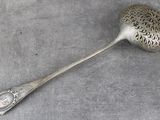 une cuillère ancienne en argent avec un manche, posée sur une surface grise