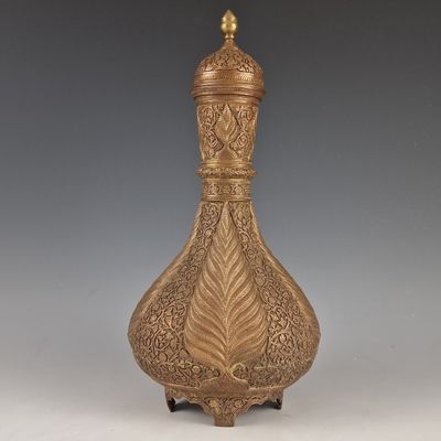 un vase ancien en laiton orné d'un motif décoratif, posé sur un socle