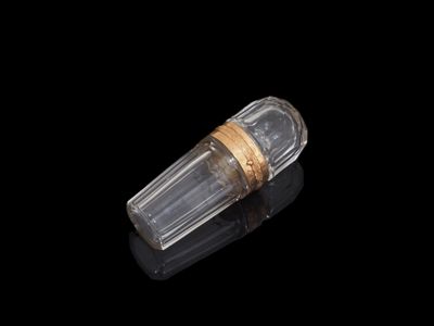 une image représentant une bouteille en verre transparent ornée d'une bande dorée, posée sur un fond noir