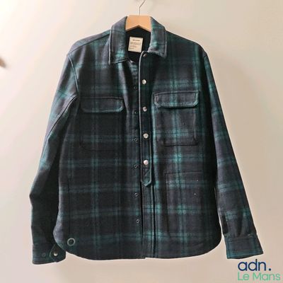 une chemise à carreaux verts et noirs accrochée à un mur