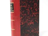 an old red and black book sitting on top of a white surface