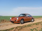 an orange porsche parked on a dirt road in front of a field