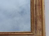 a gold framed mirror on the wall with a sky in the background