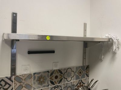 une étagère en acier inoxydable au-dessus d'une cuisinière, sur laquelle sont posées des casseroles et des poêles