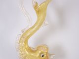 une figurine en verre représentant un poisson jaune, posée sur un socle