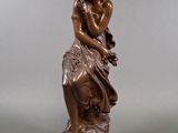 an antique bronze statue of a woman sitting on a rock