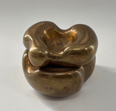 une sculpture dorée représentant un objet en forme de cœur posé sur une surface blanche