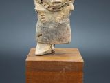 une petite statue en pierre représentant une femme, posée sur un socle en bois