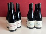 three bottles of red wine sit on a table in front of a red wall