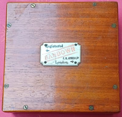 une boîte en bois avec une étiquette dessus, posée sur un fond rose