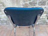a black chair with a blue seat on a brick floor